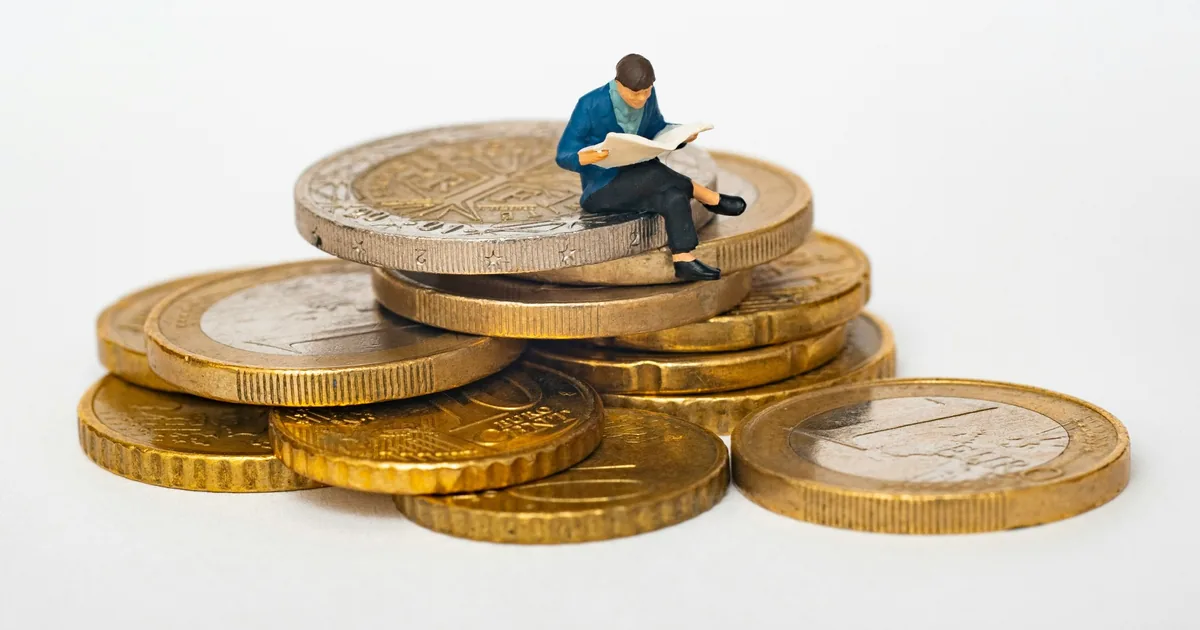 Persona leyendo sobre finanzas sentada sobre monedas: guía de bonos y renta fija de Desvío Estándar